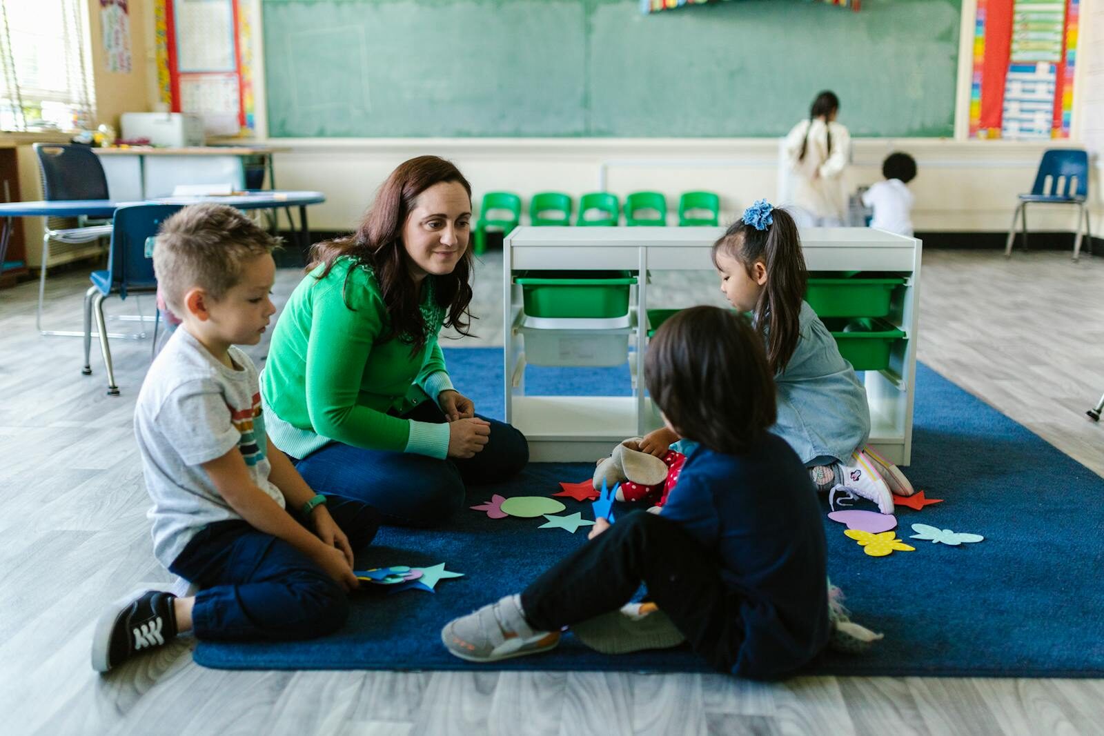 Teacher and children engaged in educational activities on a classroom floor.