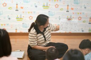 A woman holding a worksheet for children in a room with nautical wallpaper