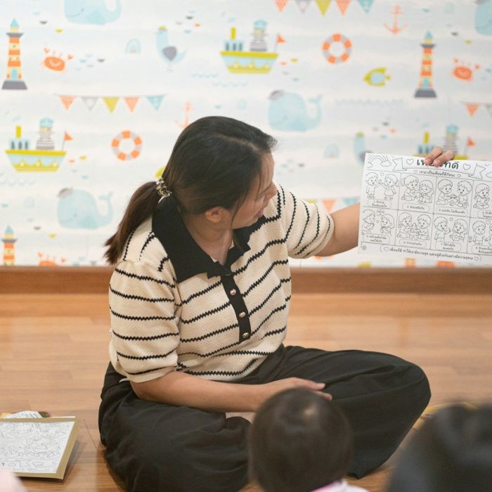 A woman holding a worksheet for children in a room with nautical wallpaper